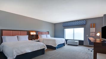 A hotel room with two beds, a desk, a chair, a TV, and a large window.