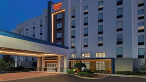 Un hotel moderno con un llamativo letrero de Hampton by Hilton, una entrada acogedora y una fachada bien iluminada.