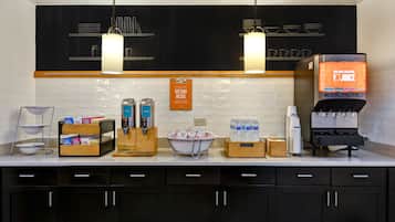 A kitchen area with a coffee machine, water dispenser, and various food items on the counter.