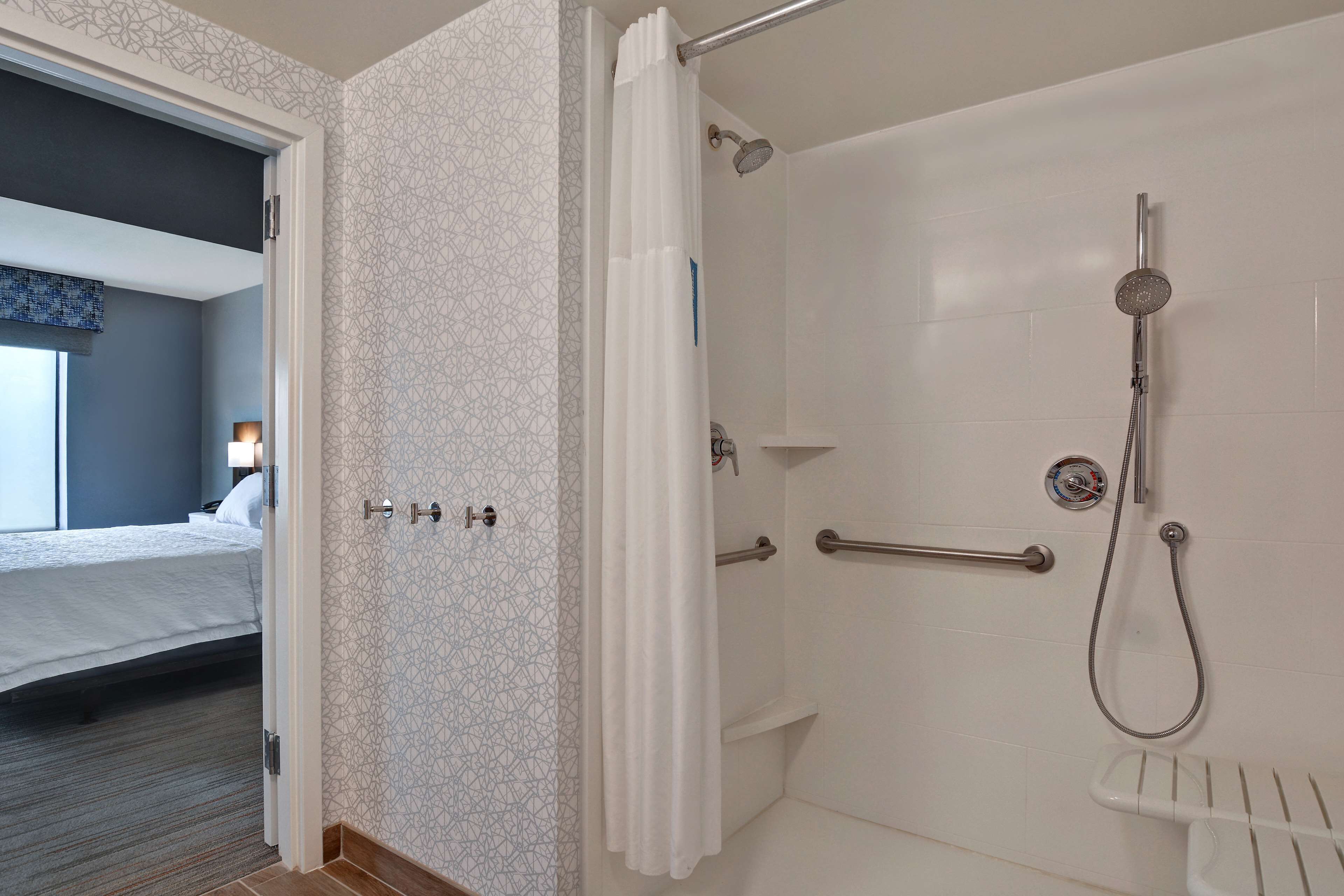 A hotel bathroom with a shower, a toilet, and a handrail.