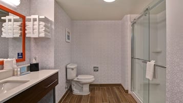 Une salle de bain moderne avec un grand miroir, des toilettes, une douche avec une porte en verre et un meuble-lavabo avec un évier et un porte-serviettes.