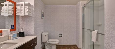 Un baño moderno con un espejo grande, un inodoro, una ducha con puerta de cristal y un mueble de tocador con lavabo y toallero.