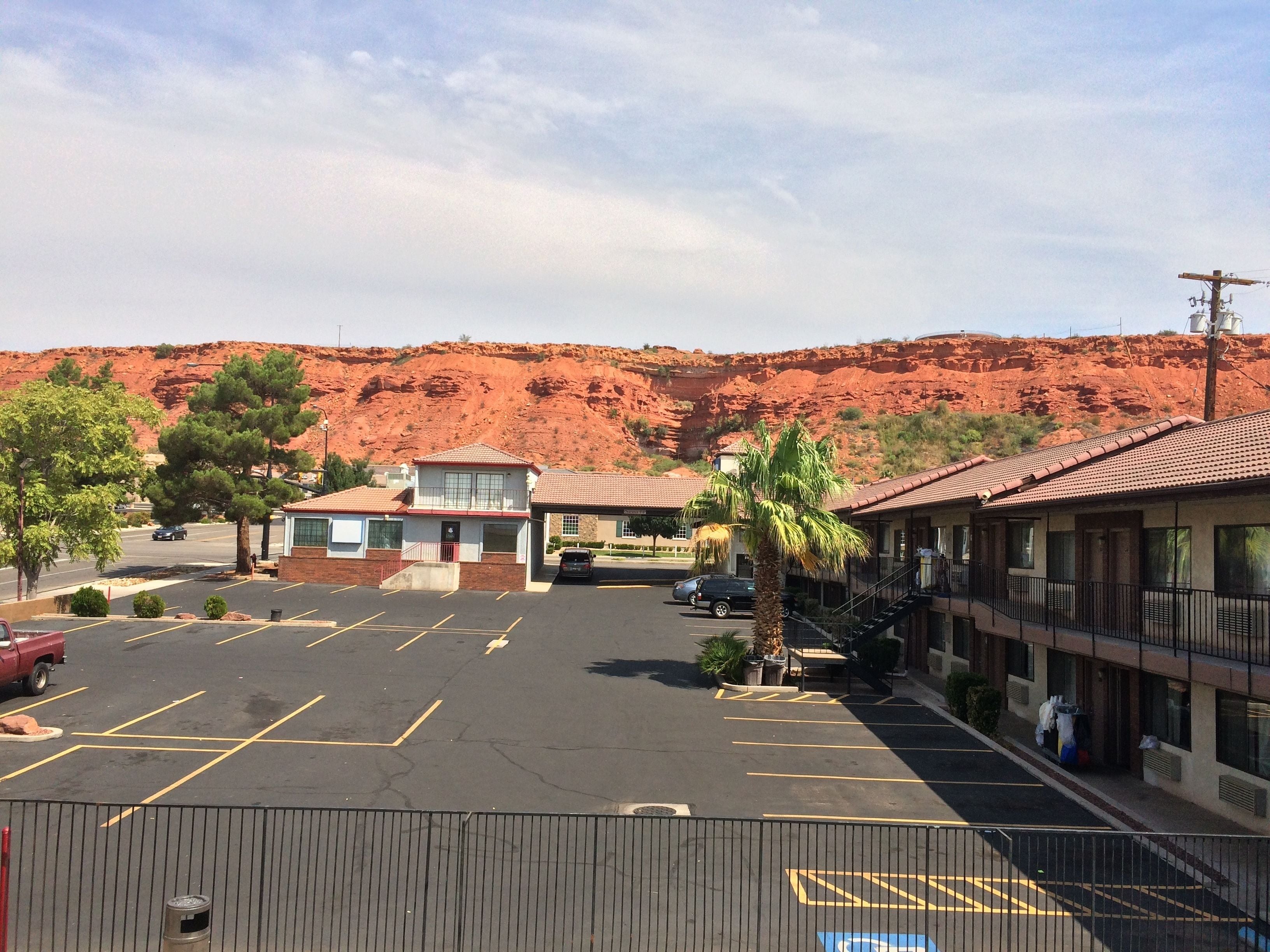 A parking lot with marked spaces, a building with a red-tiled roof, and a mountain in the background.
