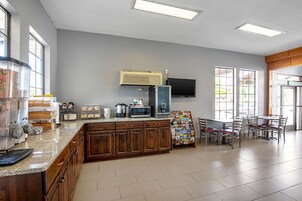 Un área de cocina con microondas, tostadora y cafetera sobre la encimera. Hay un televisor montado en la pared y una ventana con persianas.