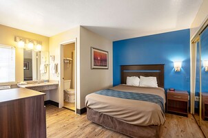 Una habitación de hotel con cama, mesita de noche y baño con lavabo e inodoro.
