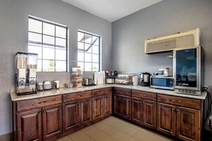 Una cocina con armarios de madera, microondas, cafetera y ventana con vistas a la vegetación.