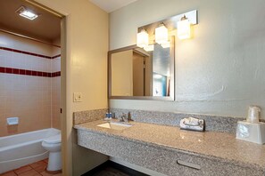 Un baño con inodoro blanco, lavabo con encimera de granito y espejo con tres luces.
