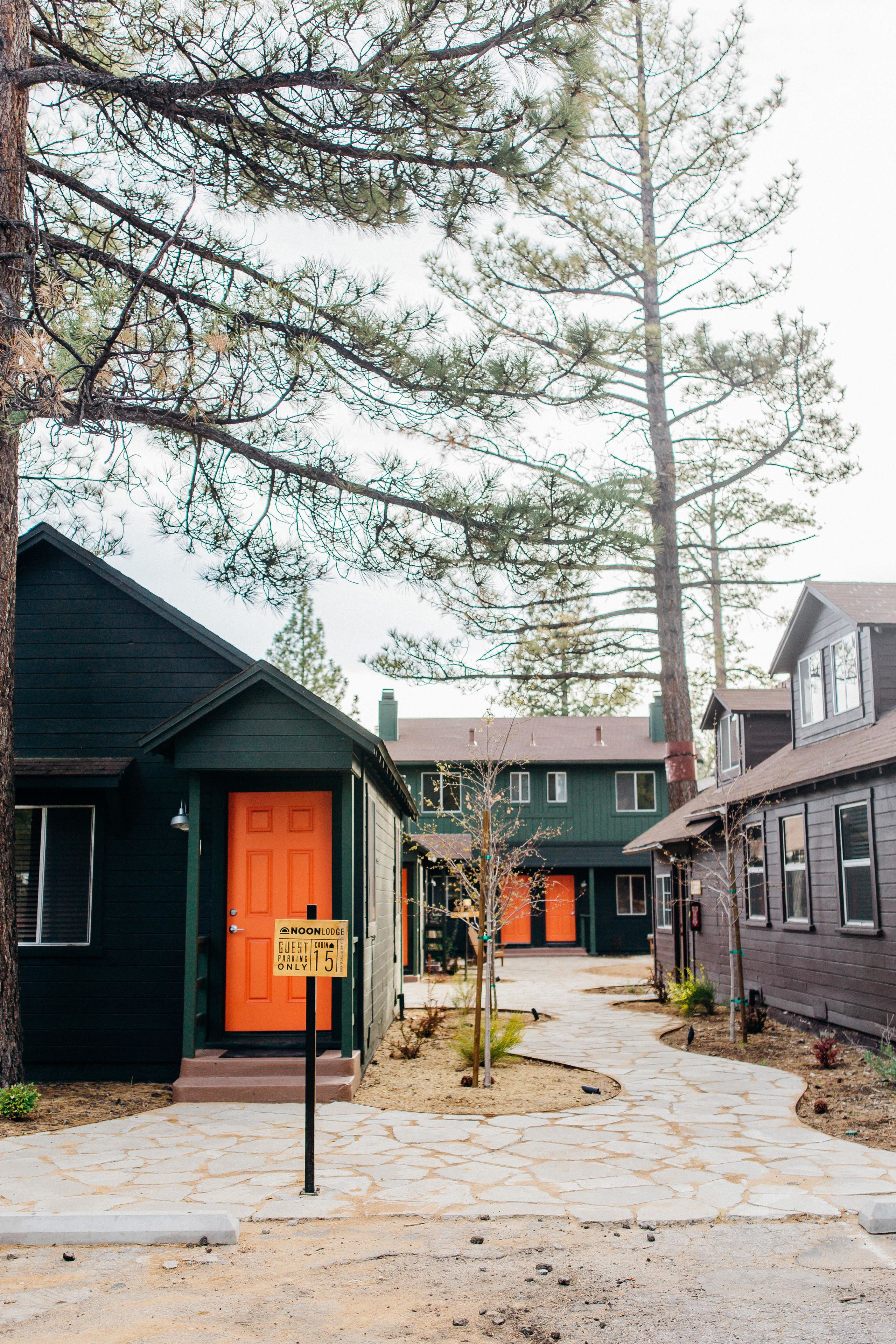 Uma fileira de casas com um caminho de pedra que leva a uma porta verde com a placa 'Noon Lodge'.