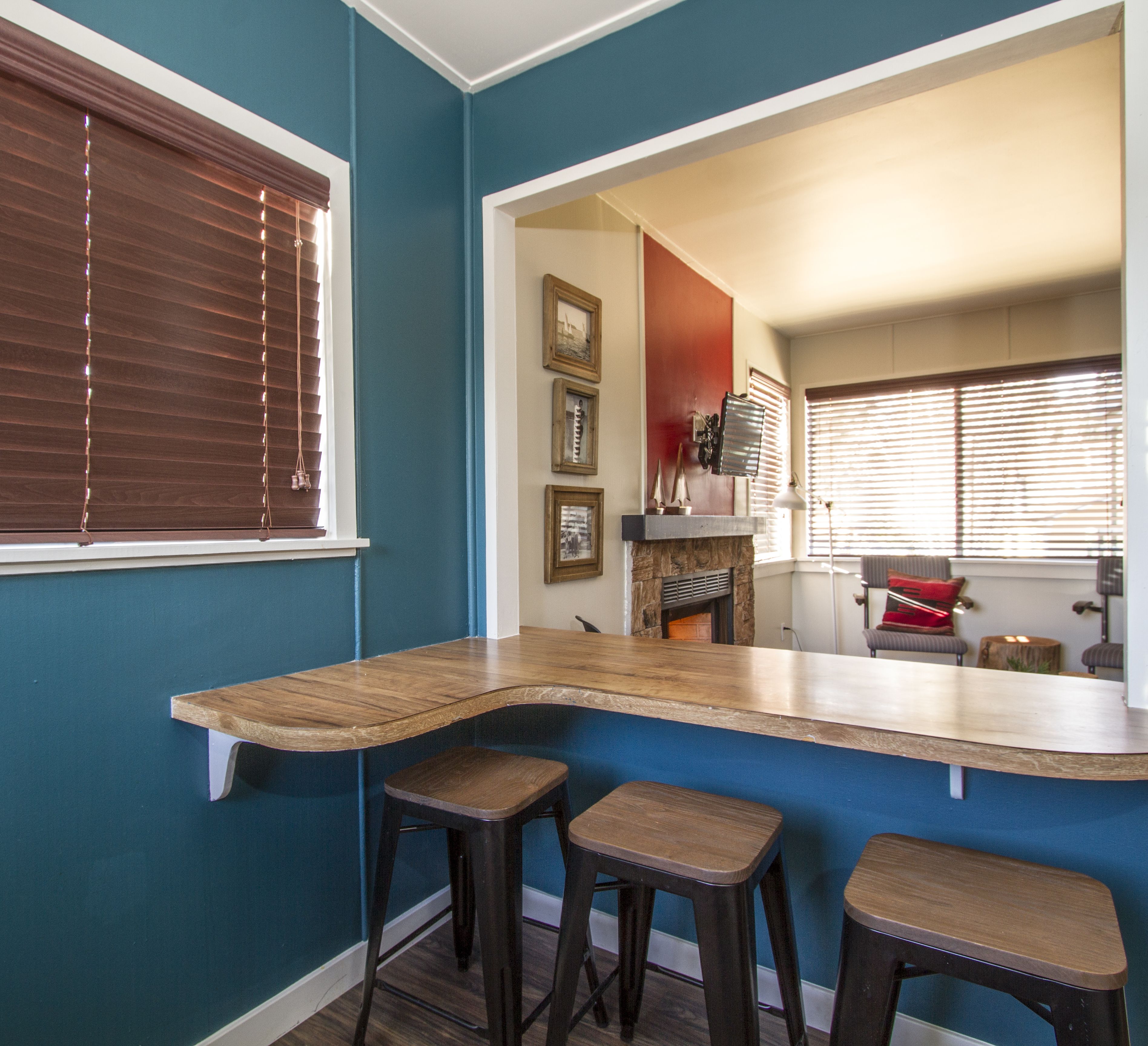 A kitchen with a curved counter, three stools, and a window with blinds.