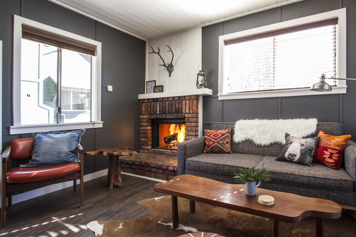 Un salon chaleureux avec une cheminée, un canapé agrémenté de coussins à motifs, une table basse en bois et un fauteuil en cuir.