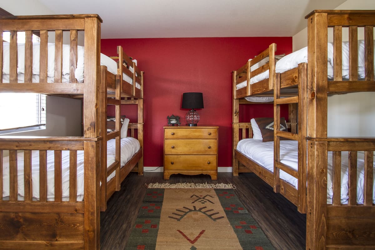 Une chambre avec deux lits superposés, une commode en bois, une lampe et un tapis à motifs.