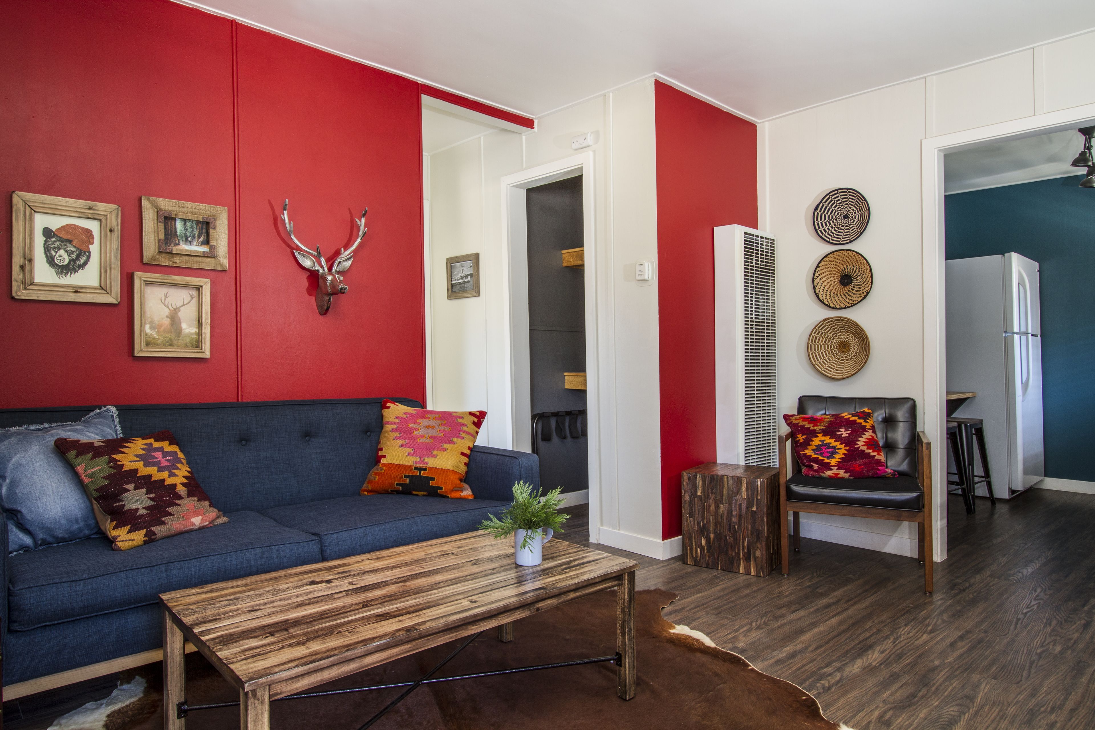 A modern living room with a blue sofa, a wooden coffee table, and a red accent wall.