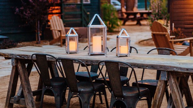 Un espacio para comer al aire libre con una mesa y sillas de madera, rodeado de árboles y una estructura que recuerda a una cabaña.