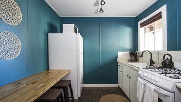 Una cocina compacta con paredes verde azulado, un refrigerador blanco, una estufa y una mesa de madera con taburetes.