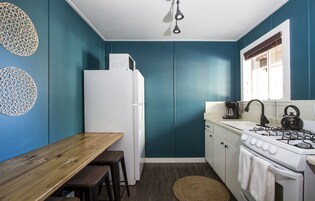 Una cocina compacta con paredes verde azulado, un refrigerador blanco, una estufa y una mesa de madera con taburetes.