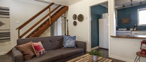 A living room with a wooden coffee table, a gray sofa with cushions, a staircase, and a kitchen area with a sign reading "CANOE RENTAL".