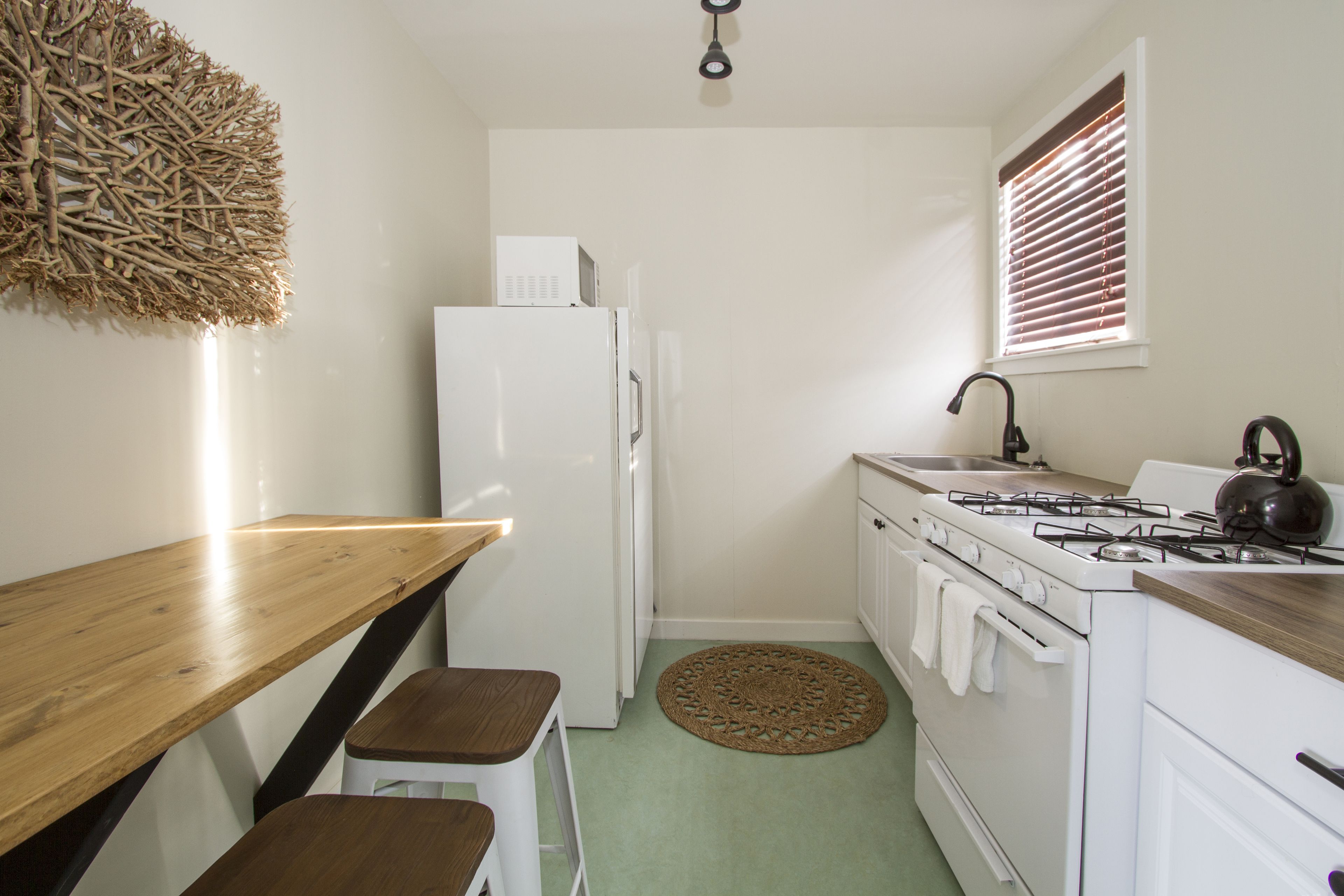 A compact kitchen with a wooden table, white cabinets, a stove, and a refrigerator.