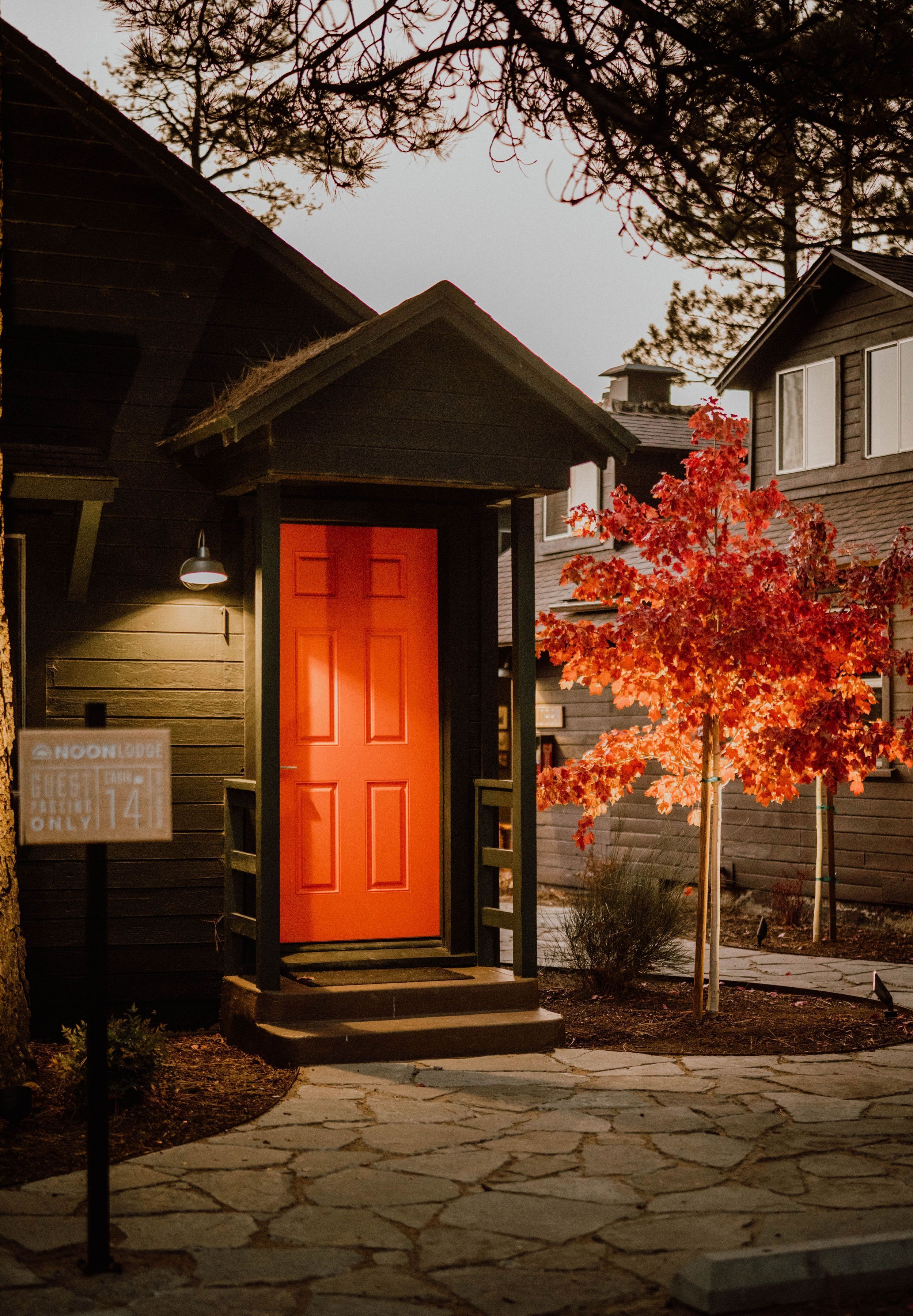Una casa de madera con una puerta roja brillante, un camino de piedra y un letrero que indica una habitación de huéspedes disponible.