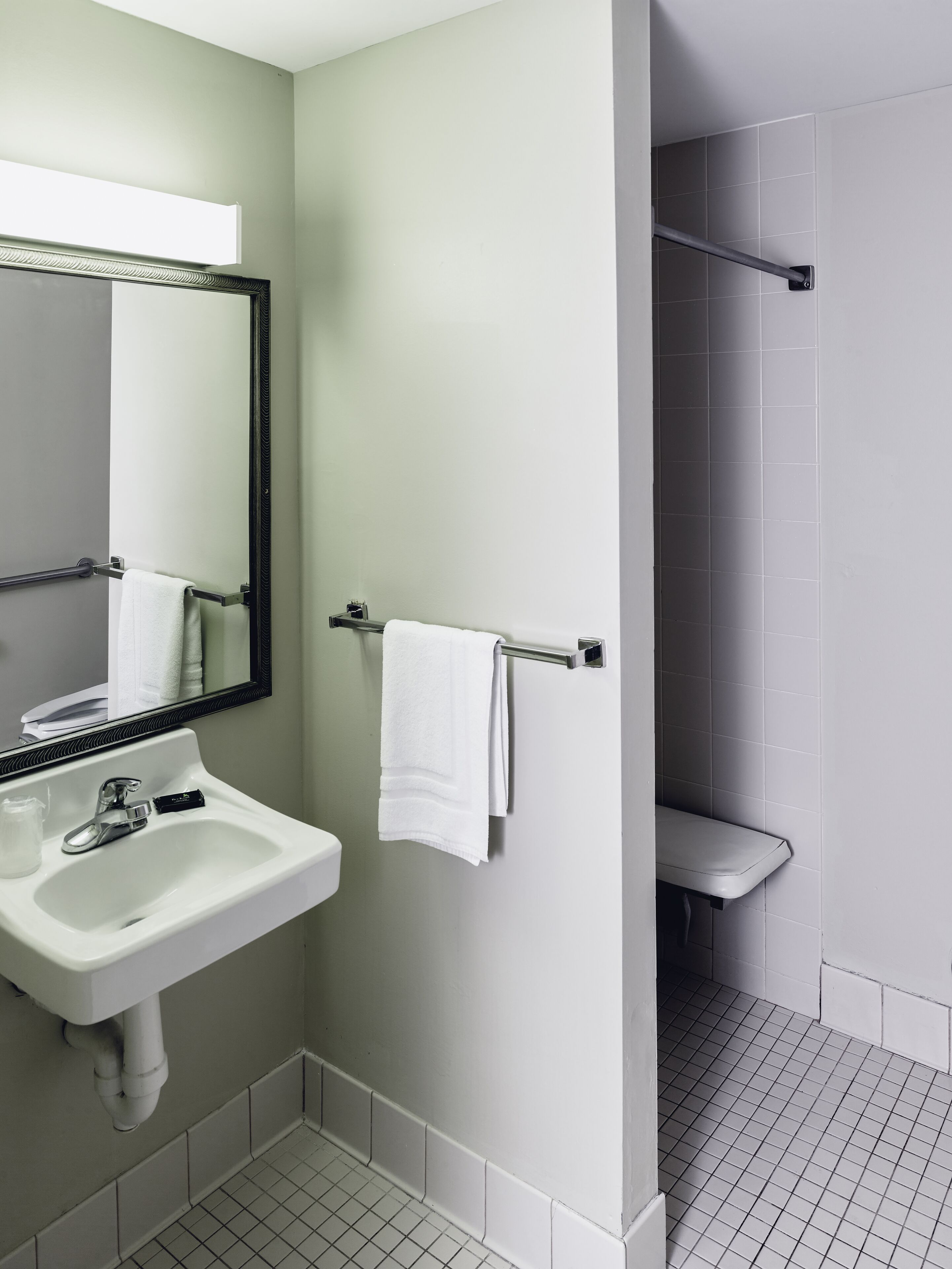 Un baño con lavamanos blanco, un espejo, toallero y zona de ducha.