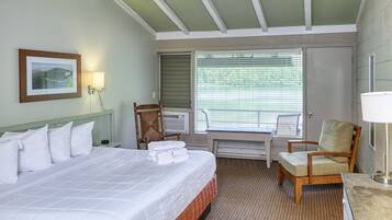 A hotel room with a bed, a chair, a desk, and a window with blinds.