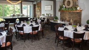 Un restaurant doté de nombreuses tables dressées pour le service, d’une cheminée en pierre et offrant une vue sur l’extérieur.