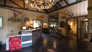 Un hall d’entrée avec un sol en pierre, un comptoir d’accueil en bois et un grand lustre orné de bois de cerf.