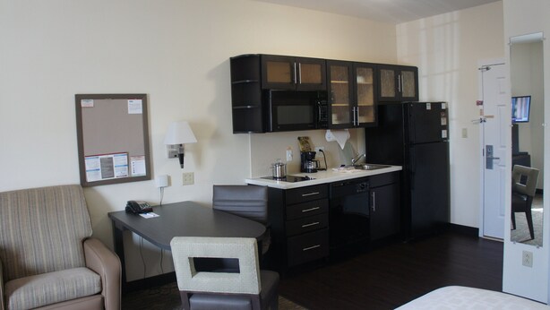 A compact hotel room with a kitchenette, a dining area, and a bed.