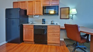 A compact kitchen with wooden cabinets, a black refrigerator, a microwave, a dishwasher, and a small desk with a chair.