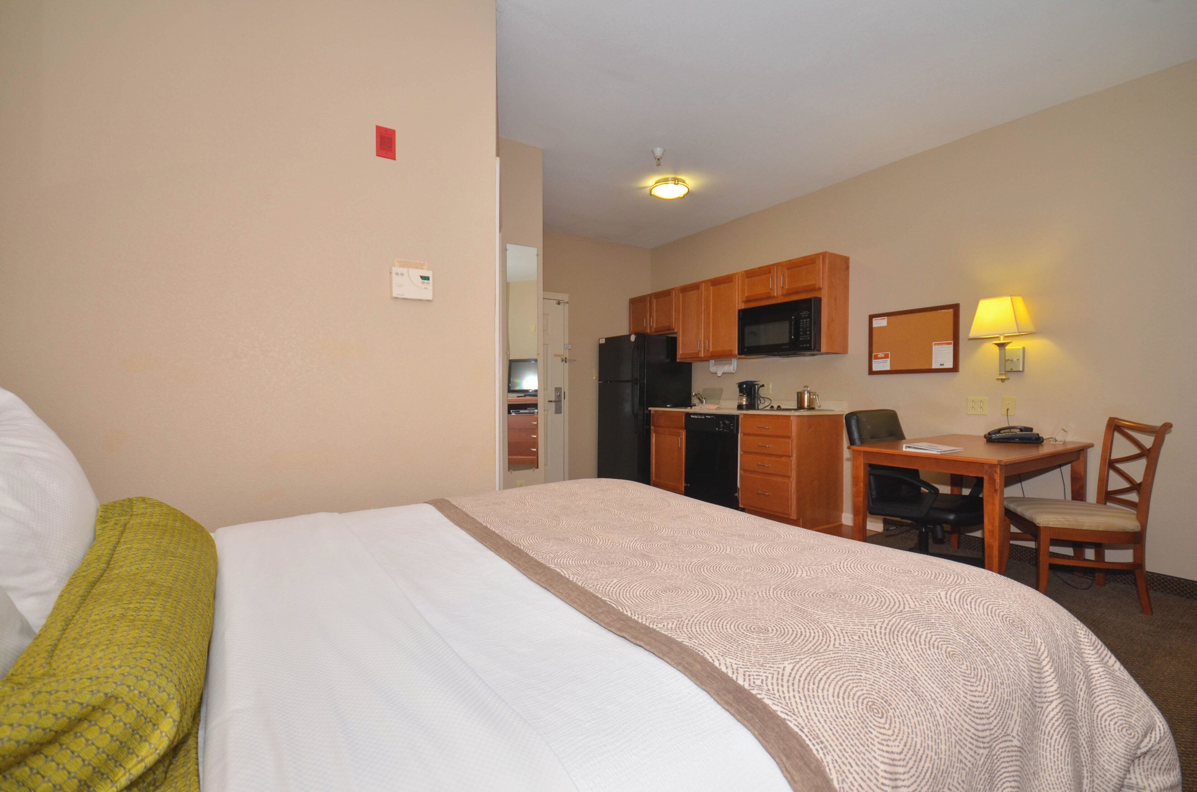 A hotel room with a bed, a desk, a chair, a microwave, and a refrigerator.
