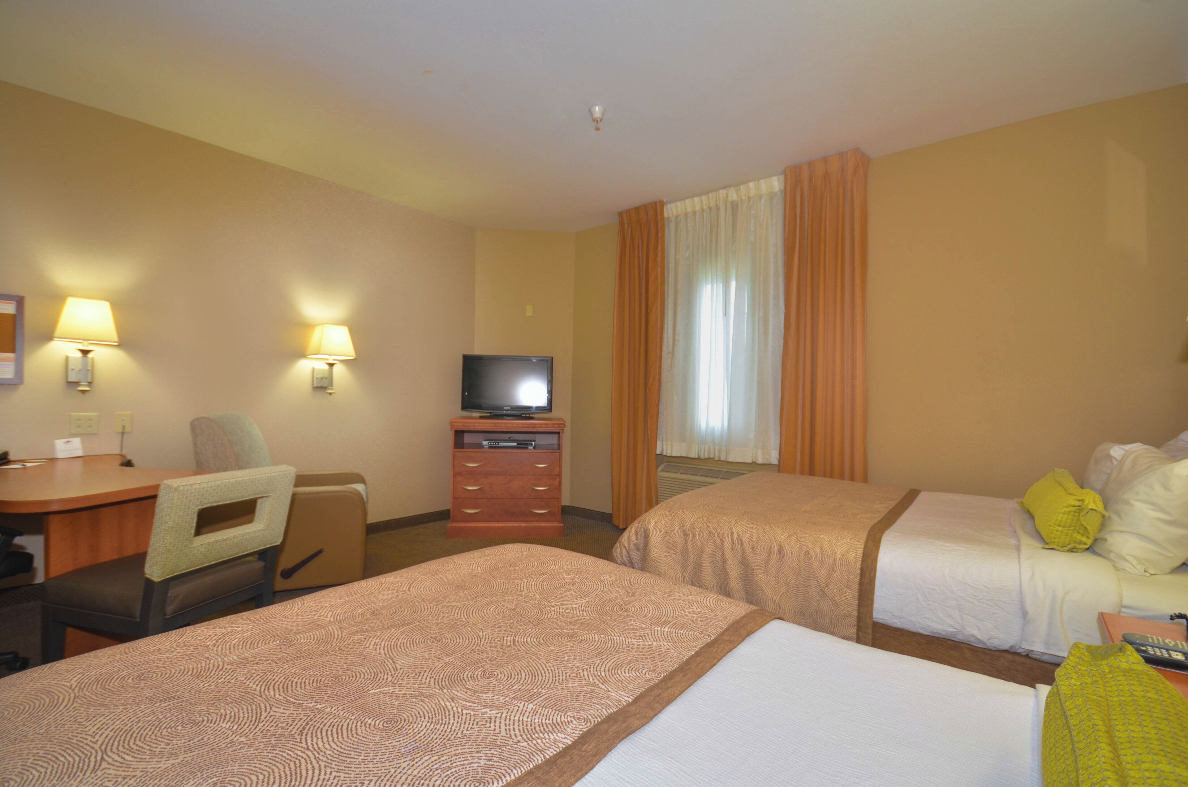 A hotel room with two beds, a desk, a chair, a television, and a window with curtains.