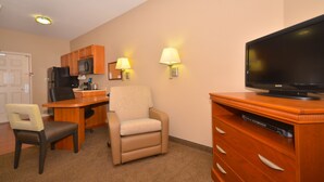A hotel room with a kitchenette, a dining table, a sofa, a TV, and a wooden cabinet.