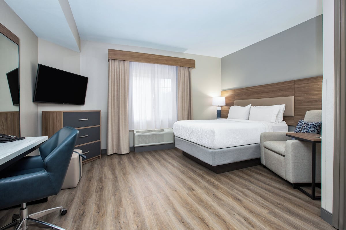 A hotel room with a bed, desk, chair, TV, and a window with curtains.