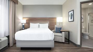 Une chambre d’hôtel moderne, dotée d’un grand lit, de lampes de chevet, d’un fauteuil et d’une salle de bain visible à travers une porte ouverte.