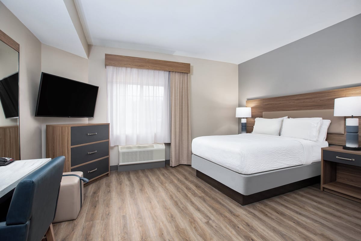 A hotel room with a bed, bedside tables, a desk, a chair, a flat-screen TV, and a window with curtains.