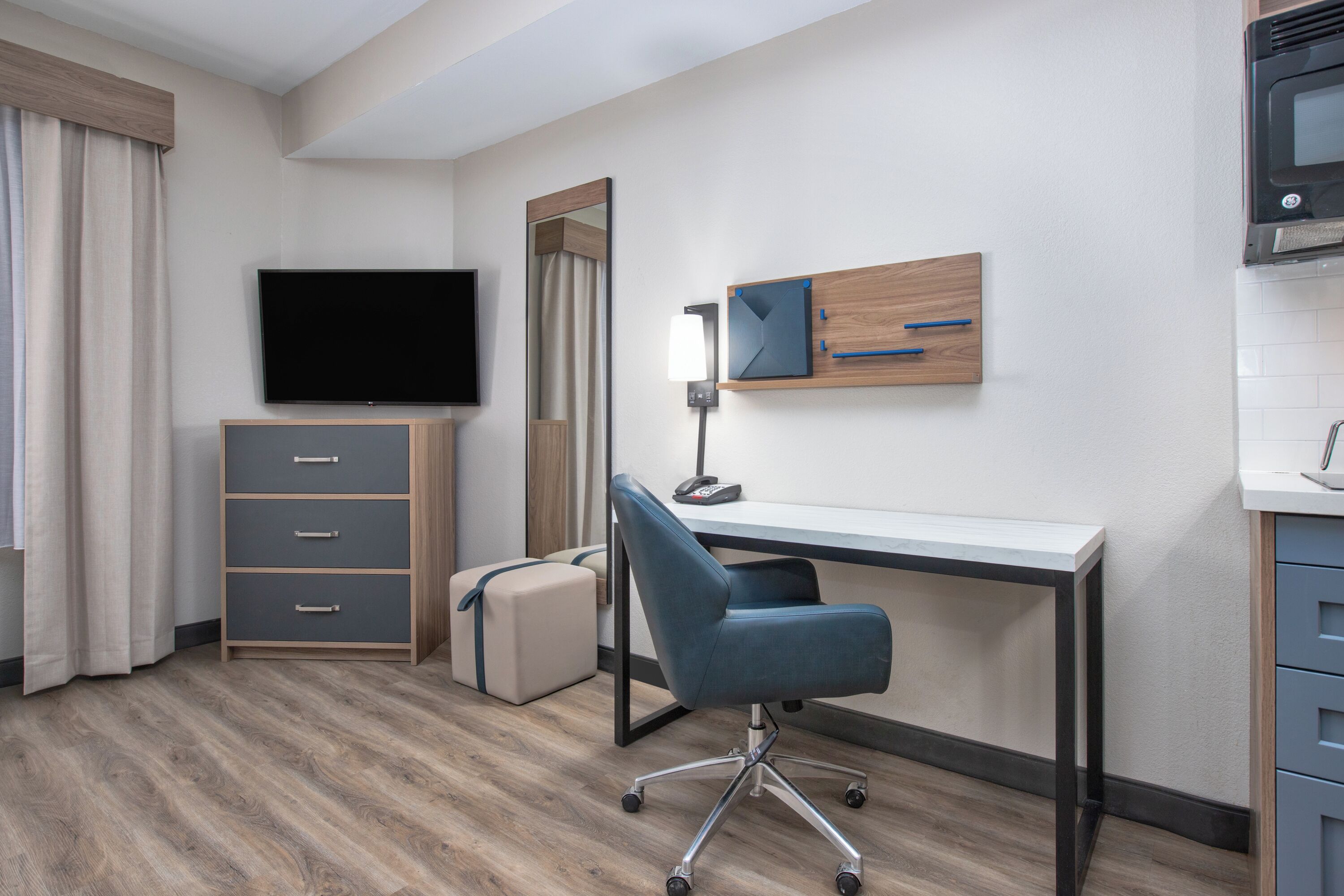 A hotel room with a desk, chair, television, wardrobe, and a small kitchenette.