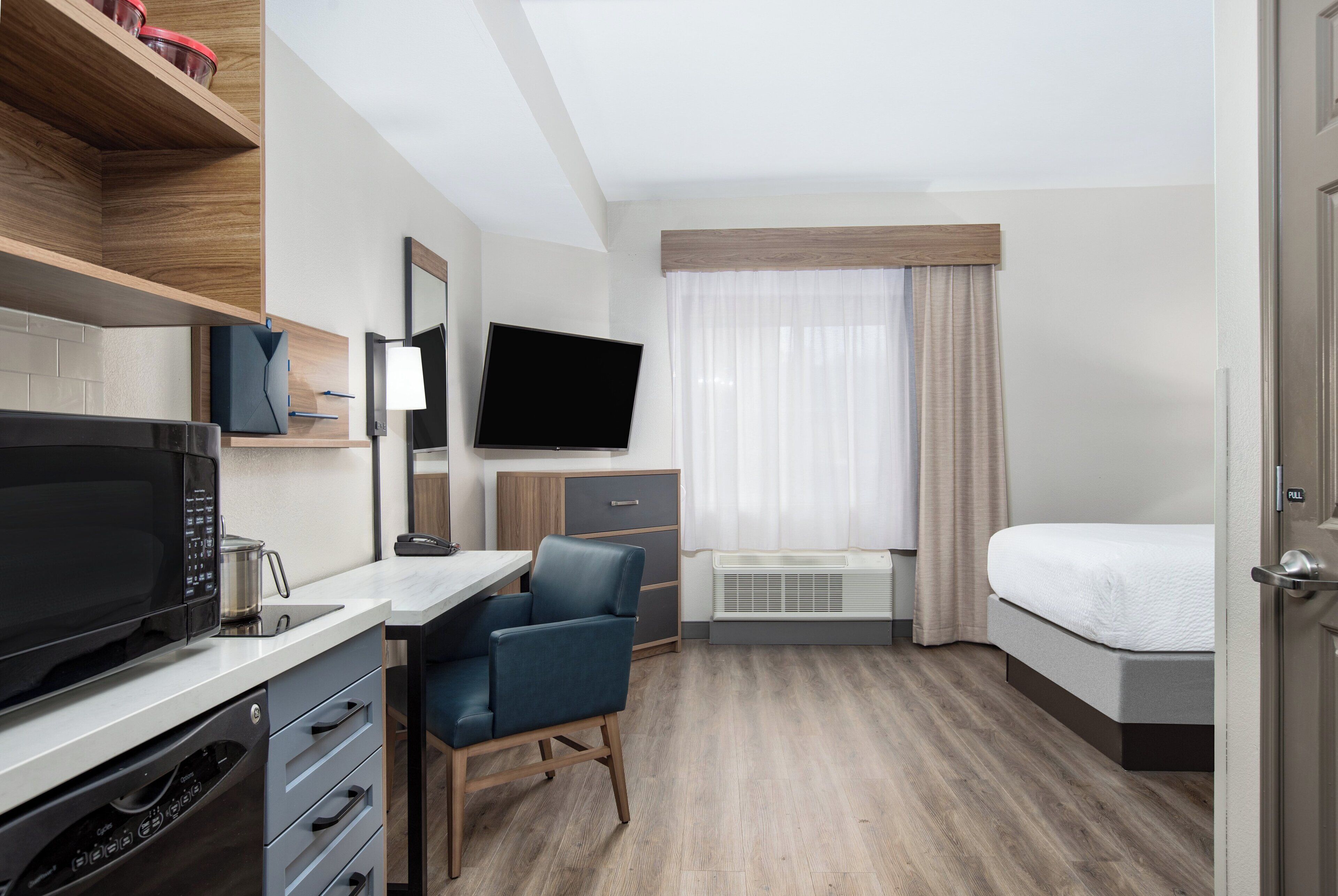 Een hotelkamer met een kitchenette, een flatscreen televisie, een bed, een bureau en een stoel.