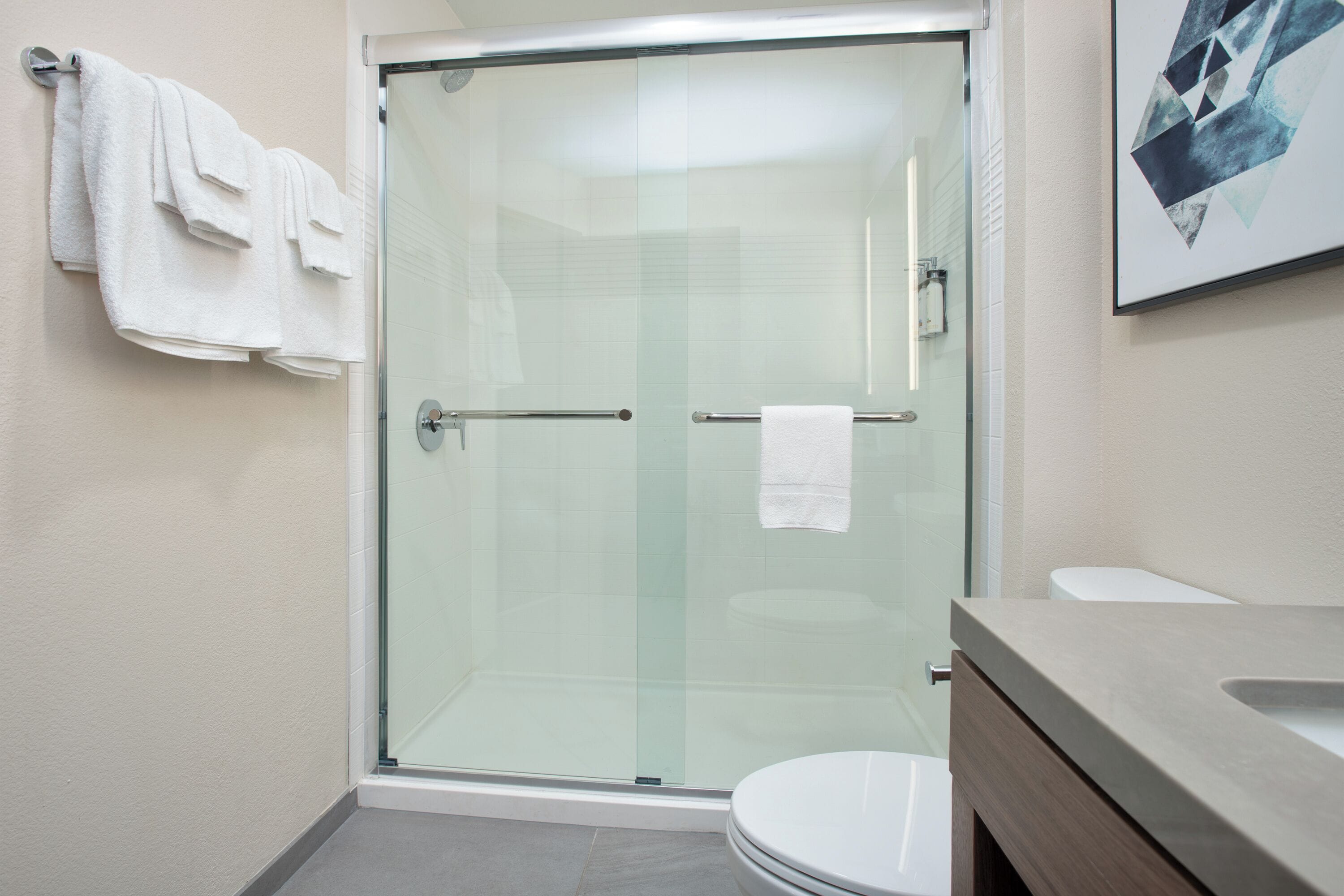 A modern bathroom with a glass-enclosed shower, a white toilet, and a beige vanity.