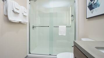 A modern bathroom with a glass-enclosed shower, a white toilet, and a beige vanity.