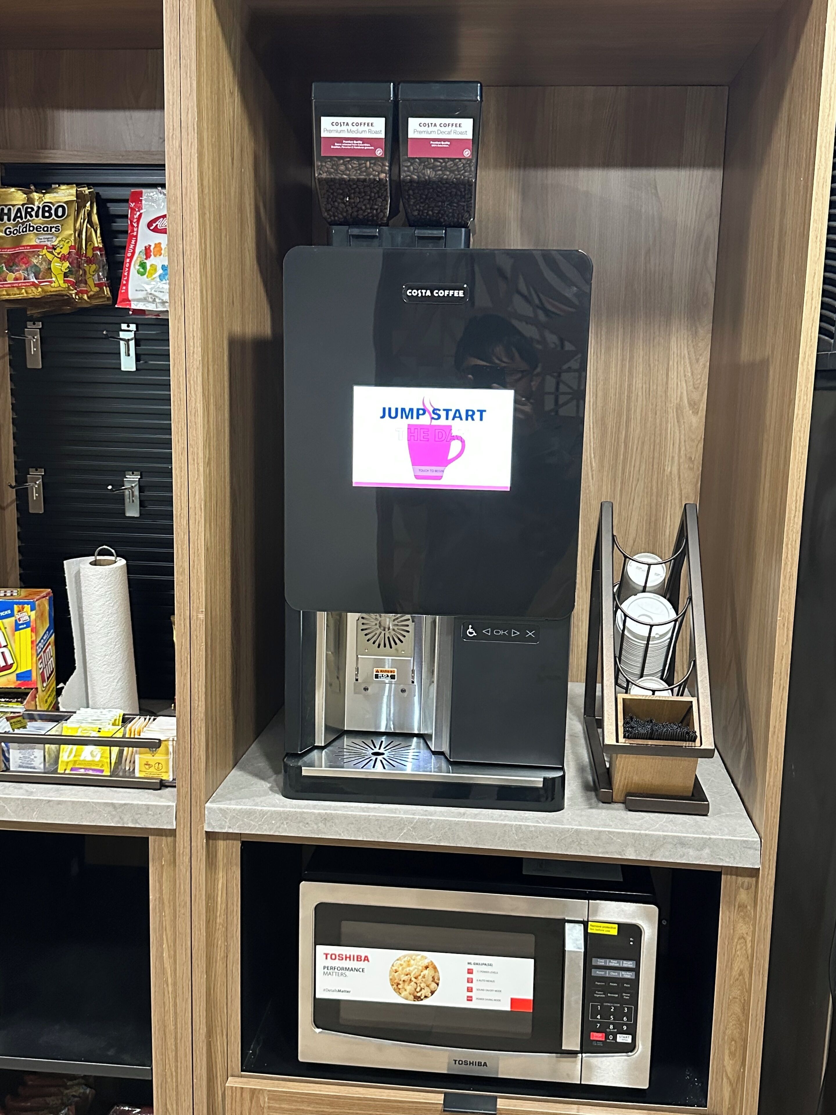 Una cafetera con pantalla digital, un molinillo de café y un microondas debajo.