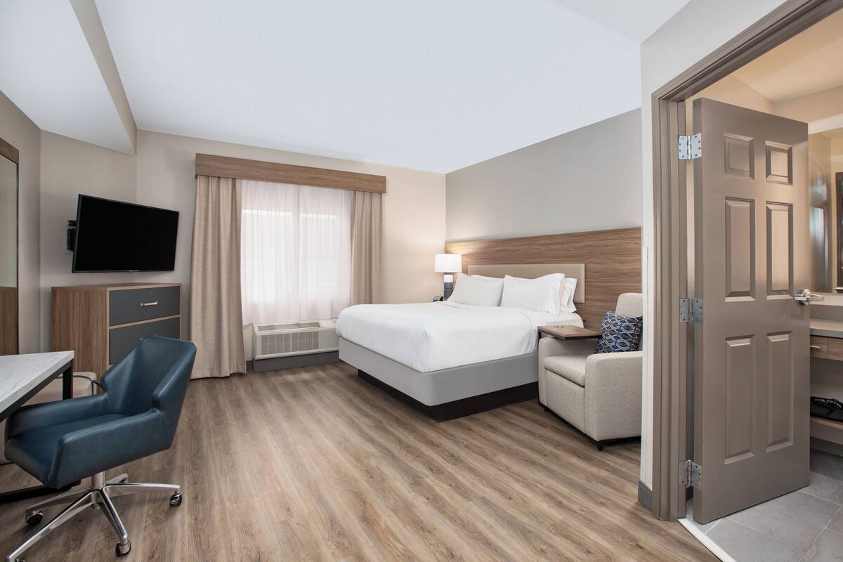 A hotel room with a bed, a desk, a chair, a TV, and a door.
