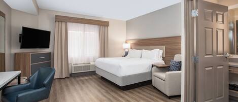 Una habitación de hotel con cama, escritorio, silla, televisor y puerta.
