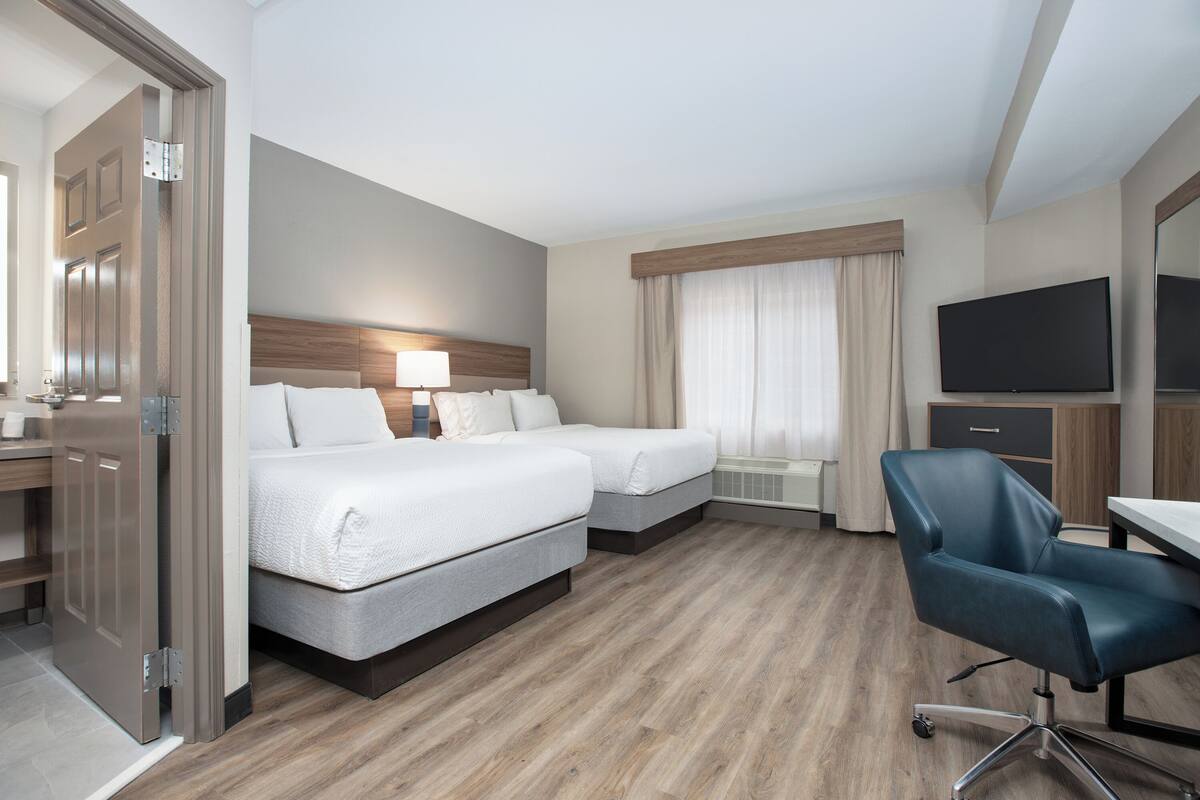A hotel room with two beds, a desk, a chair, a TV, and a wardrobe.