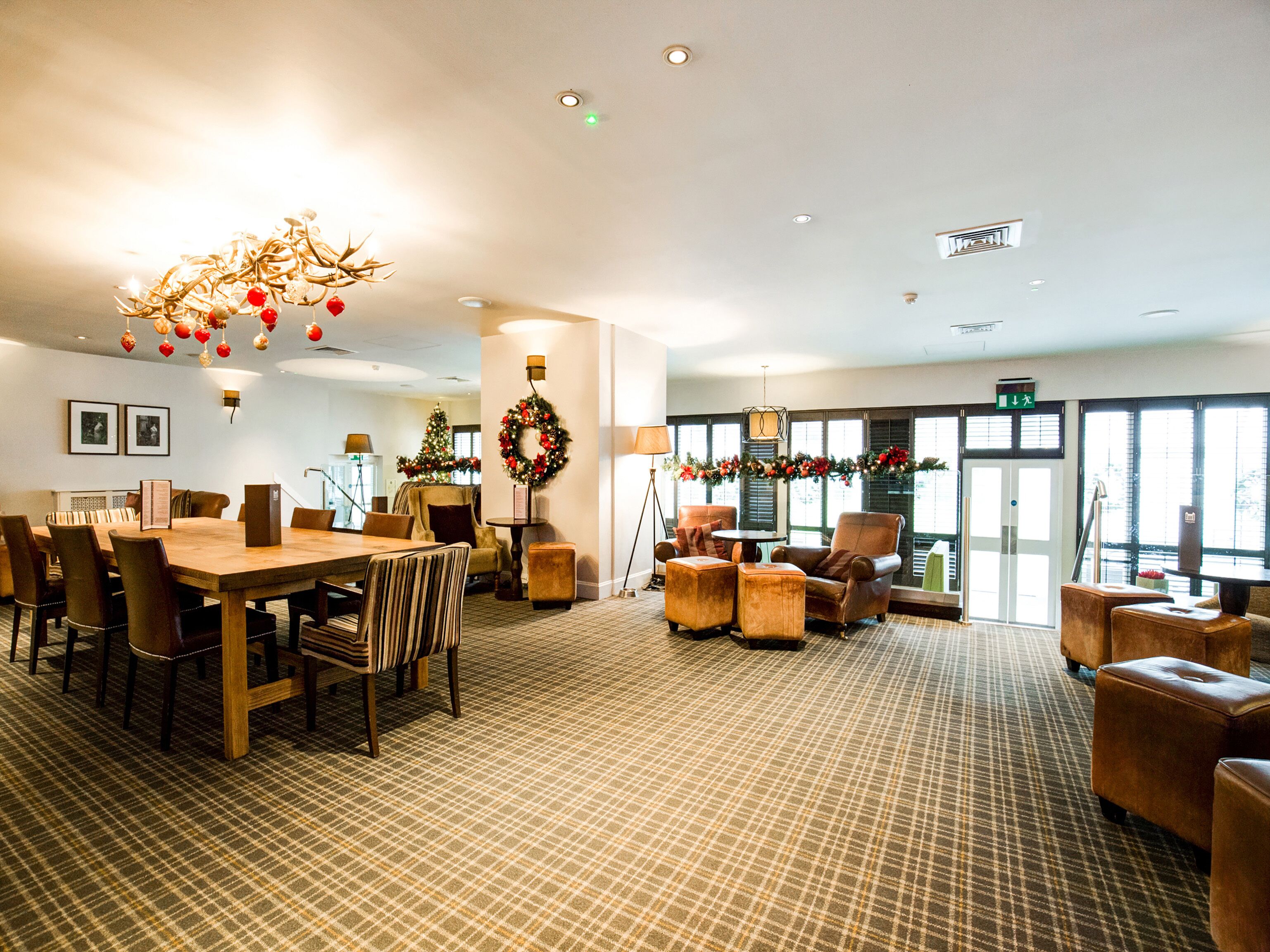 A spacious hotel lobby with a large dining table, comfortable seating, and festive decorations.