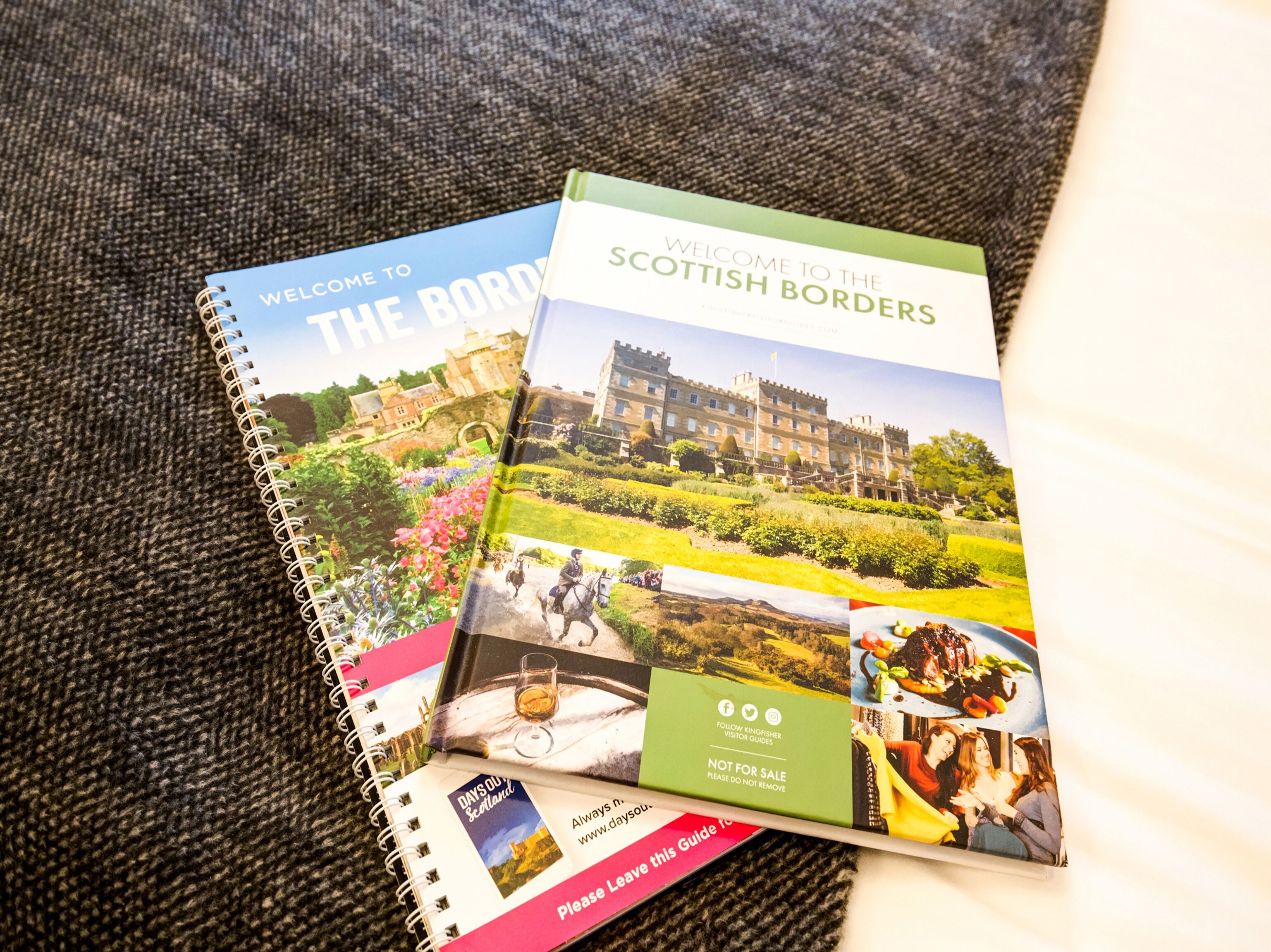 Un guide de voyage à spirale, avec de nombreuses pages visibles, dont une couverture portant le titre « Bienvenue dans les Scottish Borders » et des images de paysages et d’architecture.