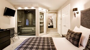 A bedroom with a large bed, a flat-screen TV, a walk-in closet, and a bathroom with a bathtub and shower.