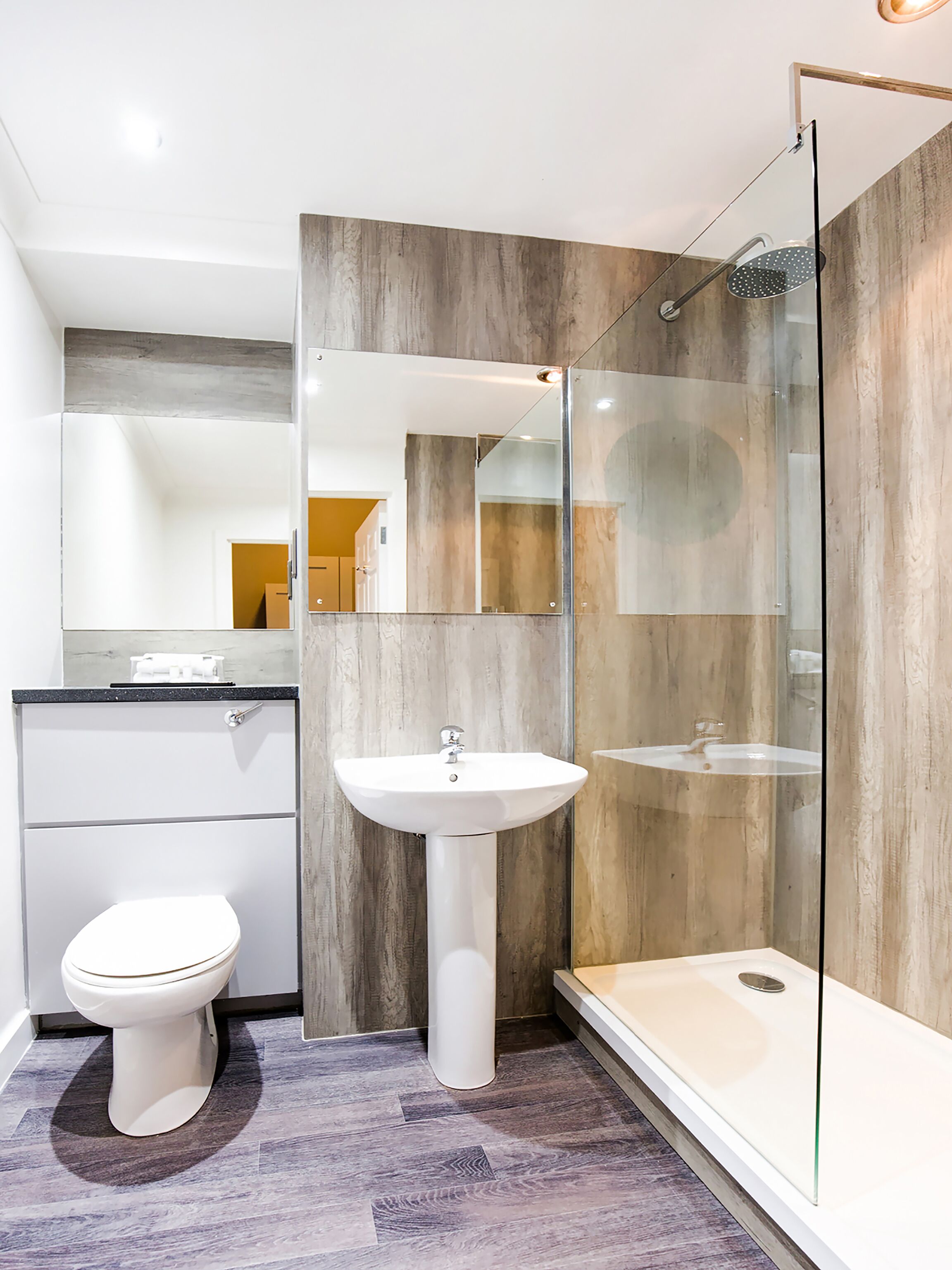 A modern bathroom with a white toilet, pedestal sink, and glass-enclosed shower.
