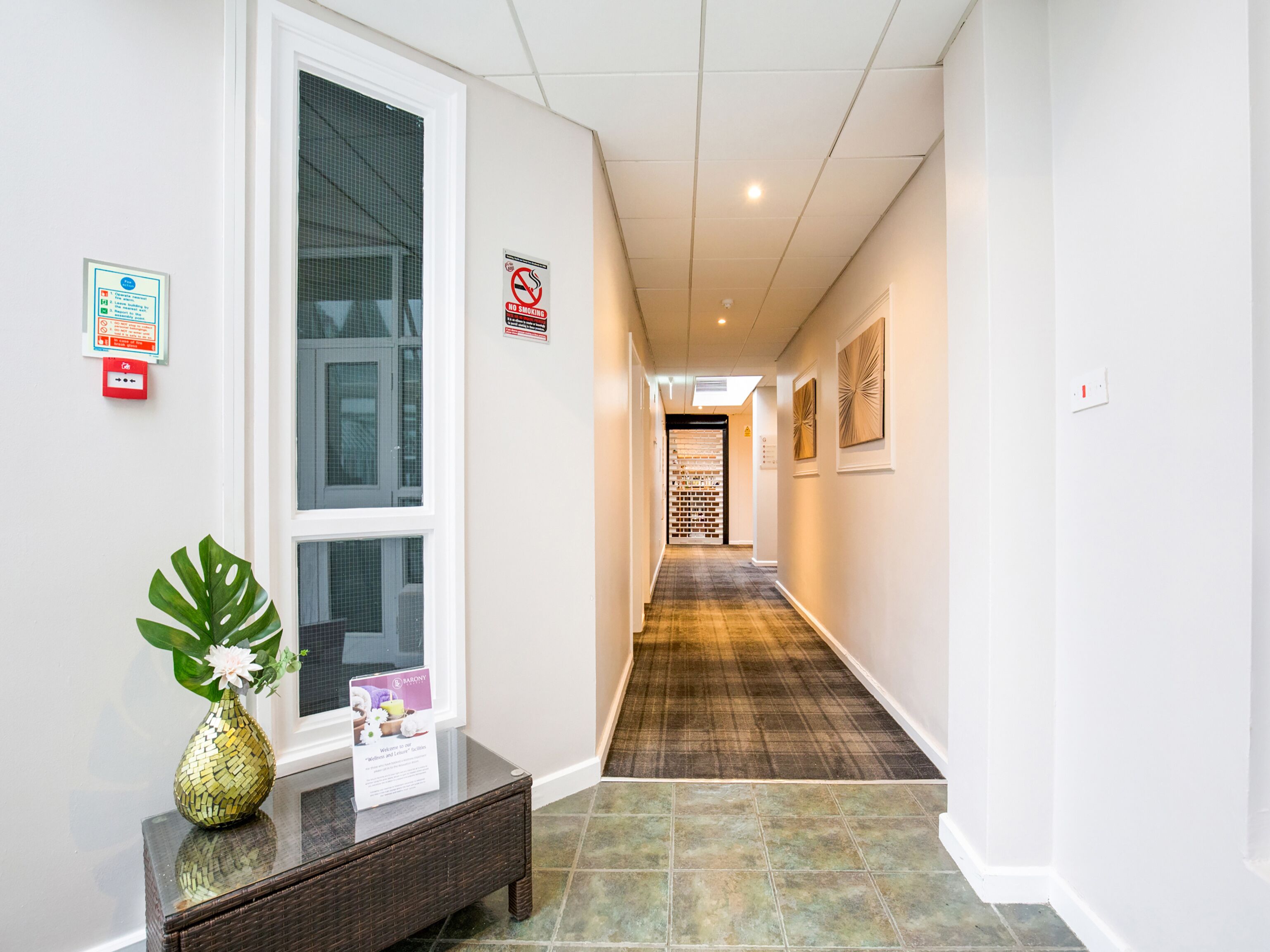A hotel hallway with a checkered floor, a no smoking sign, and a welcome sign.