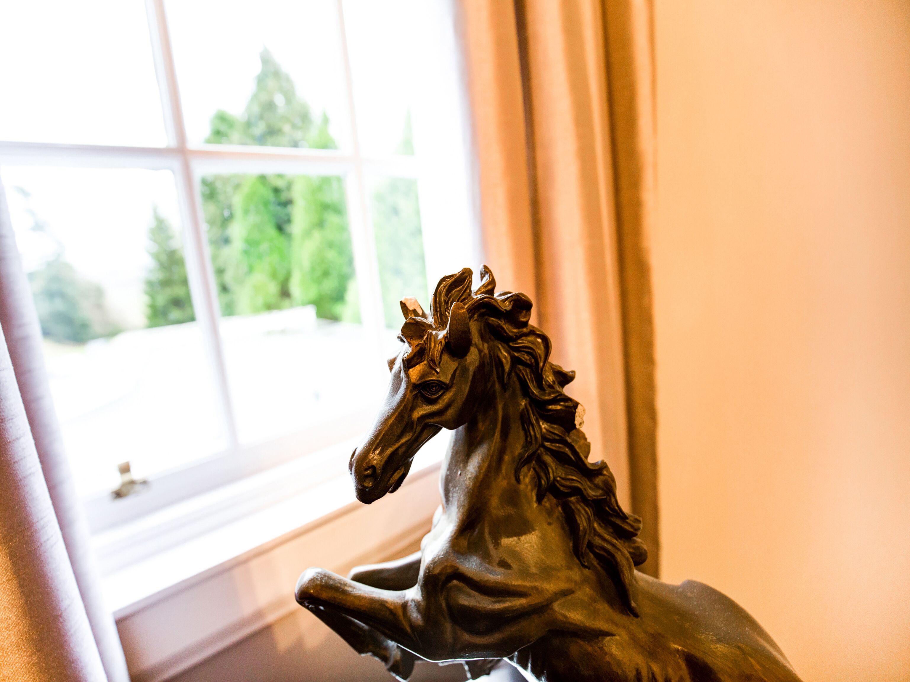 Une statue de cheval en bronze, dans une pièce avec une fenêtre.