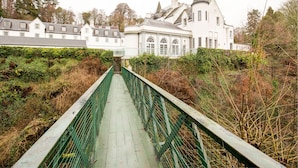 A bridge leading to a large white building with multiple windows and a tower.