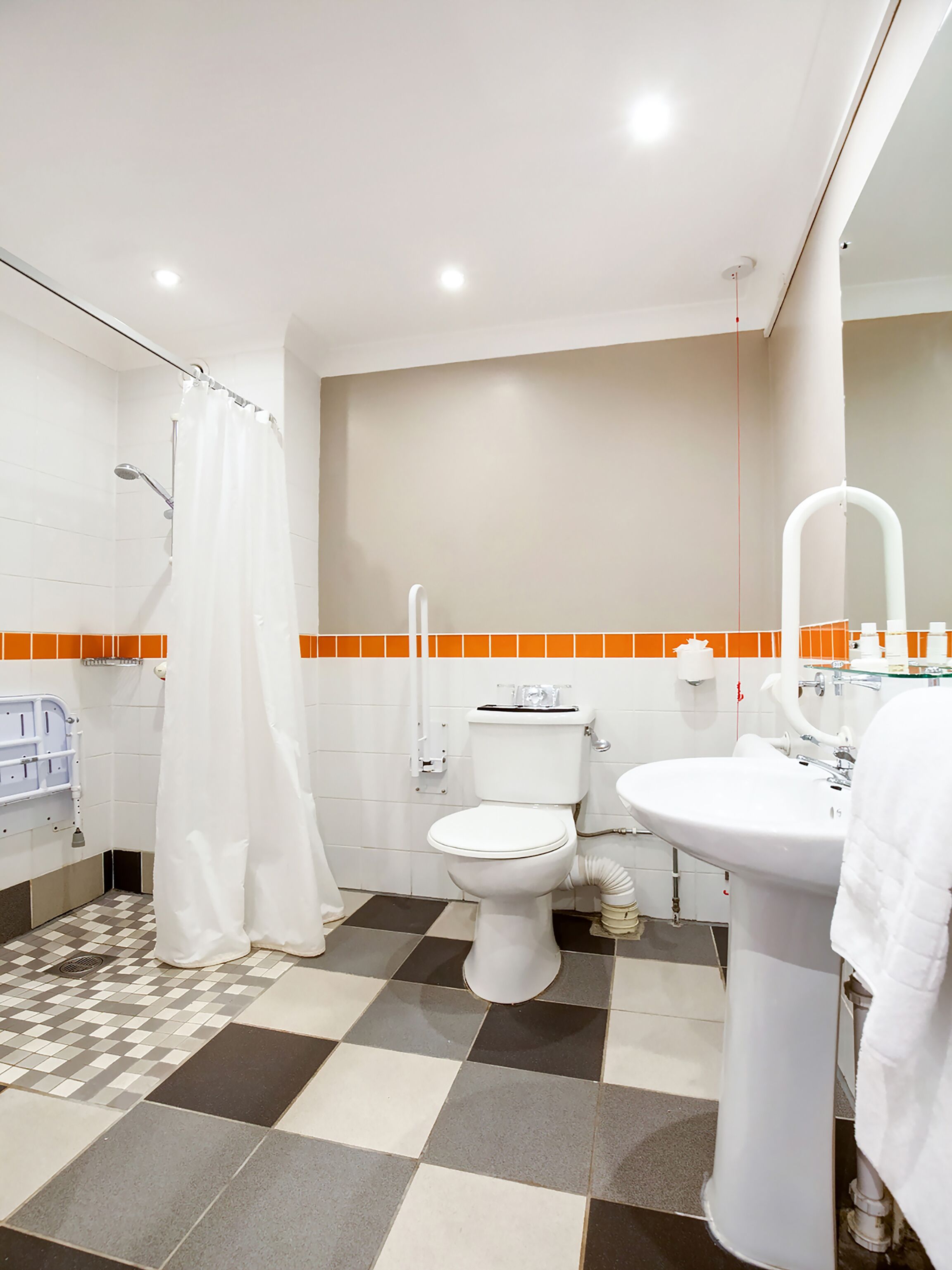 Un baño con inodoro, lavamanos y ducha. El piso tiene un diseño de cuadros.
